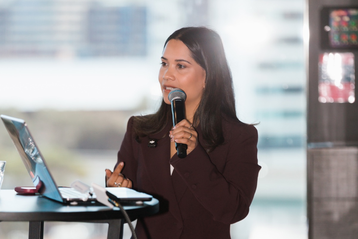 Daniela Valencia, founder of Reclaim Creative, speaking into a microphone beside a laptop while presenting an AI training session.